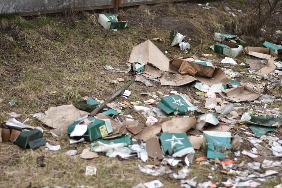 A large pile of black plastic rubbish bags, some tied and others loose, are stacked against a modern tiled wall outdoors in an urban environment. The bags appear full and bulging, containing various h
